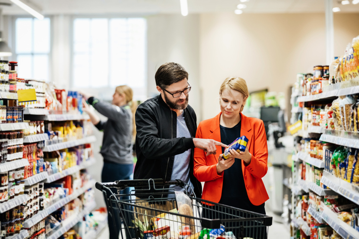 A mature couple reading the nutrition label on a food item while shopping for groceries at their local supermarket.