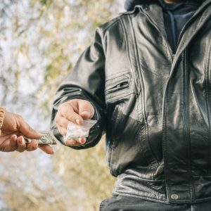 Male drug dealer sells hard drugs in a transparent plastic bag to an addicted woman with money in her hand, cropped image.